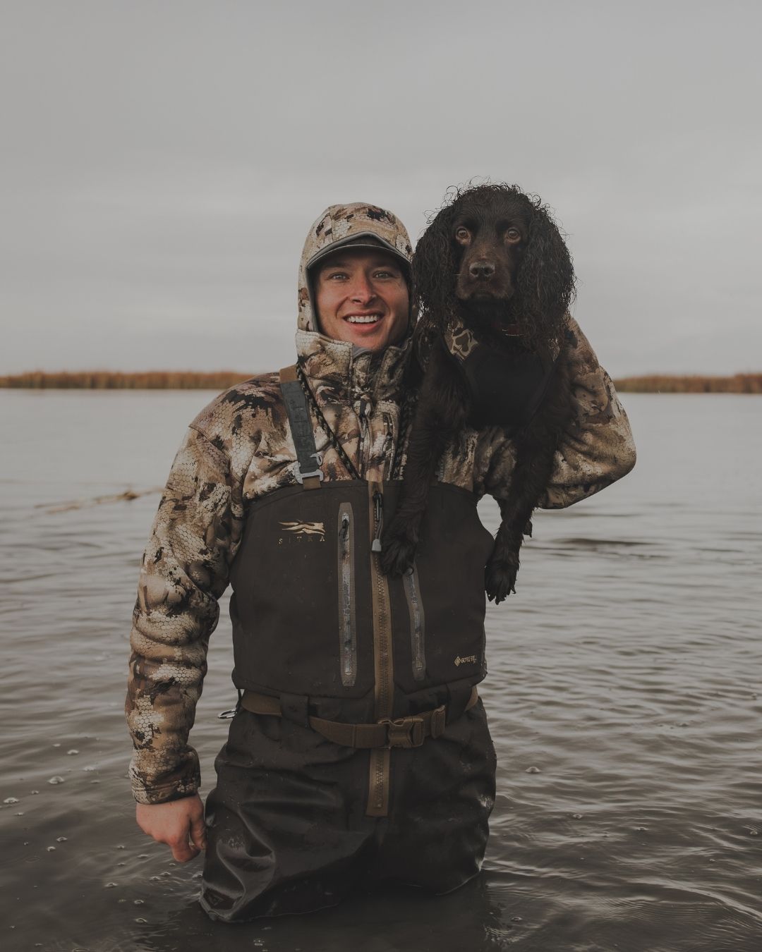 Man and Boykin Spaniel standing in thigh deep water.